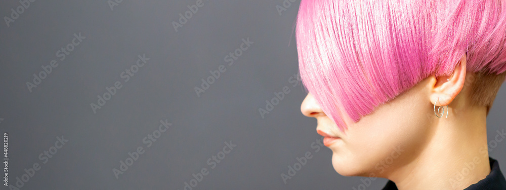 Profile portrait of a young caucasian woman with pink bob haircut isolated on a gray background, copy space