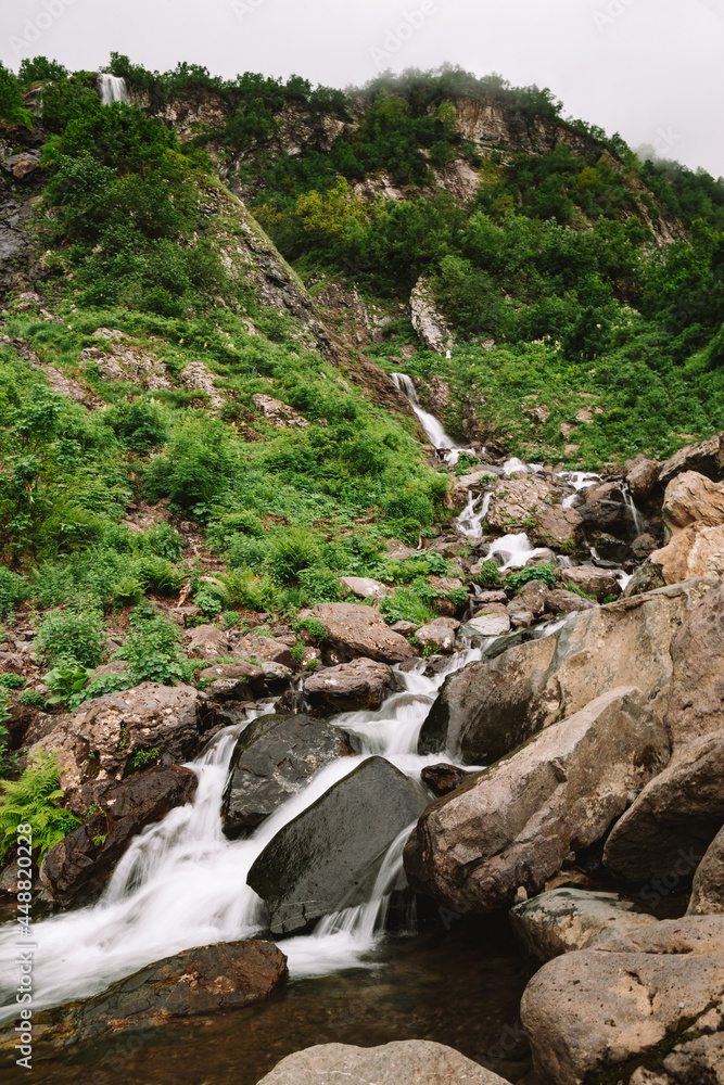 Beautiful mountain waterfall among trees, summer natural background, vertical photo Beautiful mountain waterfall among trees, summer natural background, vertical photo