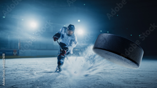 Ice Hockey Rink Arena: Professional Player Shooting the Puck with Hockey Stick. Focus on 3D Flying Puck with Blur Motion Effect. Dramatic Wide Shot, Cinematic Lighting. photo