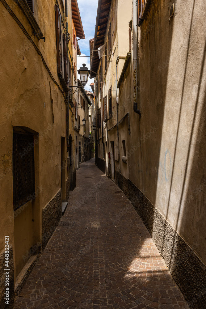 Very narrow alley in Bellano, lake Como, Lombardy, Italy. Narrow alley between the residential buildings in the small town of Bellano by the Como lake, Lombardy, Italy. Just a little sun comes down