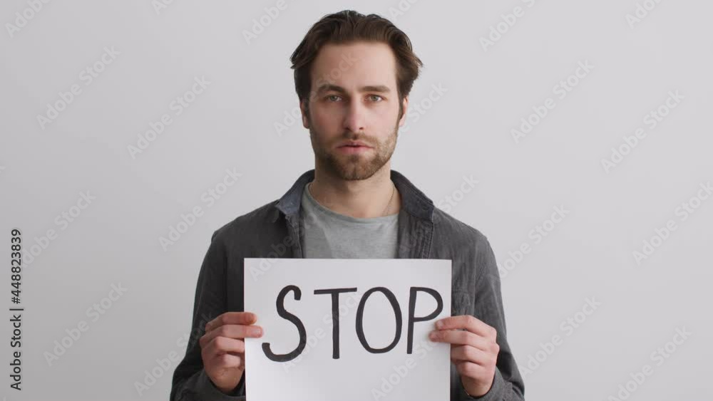 Stop global discriminations. Close up studio portrait of young sad man rising poster with word STOP Stop global discriminations. Close up studio portrait of young sad man rising poster with word STOP