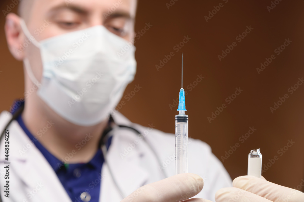 Young caucasian male doctor in a white coat holding a syringe with a vaccine. Focus on the syringe Young caucasian male doctor in a white coat holding a syringe with a vaccine. Focus on the syringe