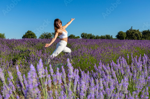 Fototapeta Naklejka Na Ścianę i Meble -  Warrior yoga pose in a blooming lavender field. A woman with long brown hair stretches the front of her body to strengthen her legs, torso and back. Sense of energy and stability.