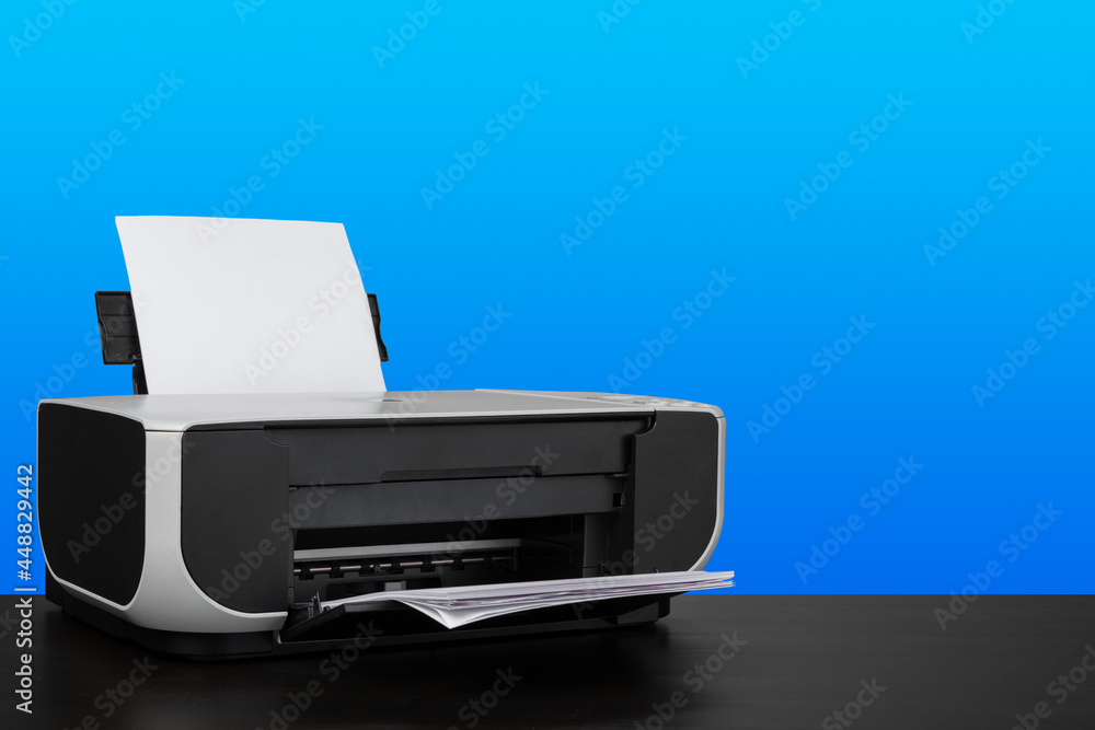 Compact laser printer on black desk against blue background Compact laser printer on black desk against blue background
