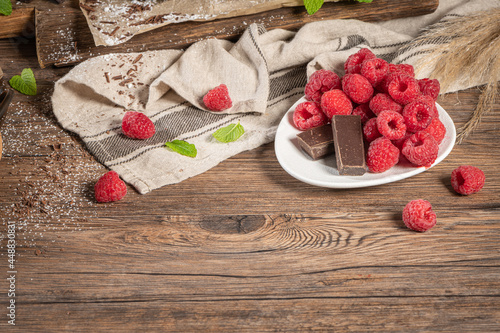 Fresh raspberry in plate. Close up red raspberries fruit and chocolate with green mint leaf on kitchen coutertop background. photo