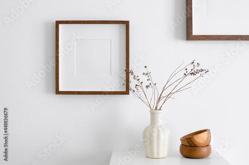 Square wooden frame mockup for artwork, photo, print and painting presentation. White walll with vase, dry twigs and wooden decorations.