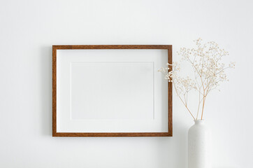 Landscape wooden frame mockup with copy space for artwork, photo or print presentation. White wall and vase with dry gypsophila flower decoration.