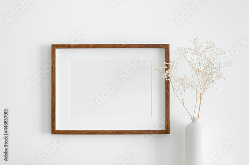 Landscape wooden frame mockup with copy space for artwork, photo or print presentation. White wall and vase with dry gypsophila flower decoration.