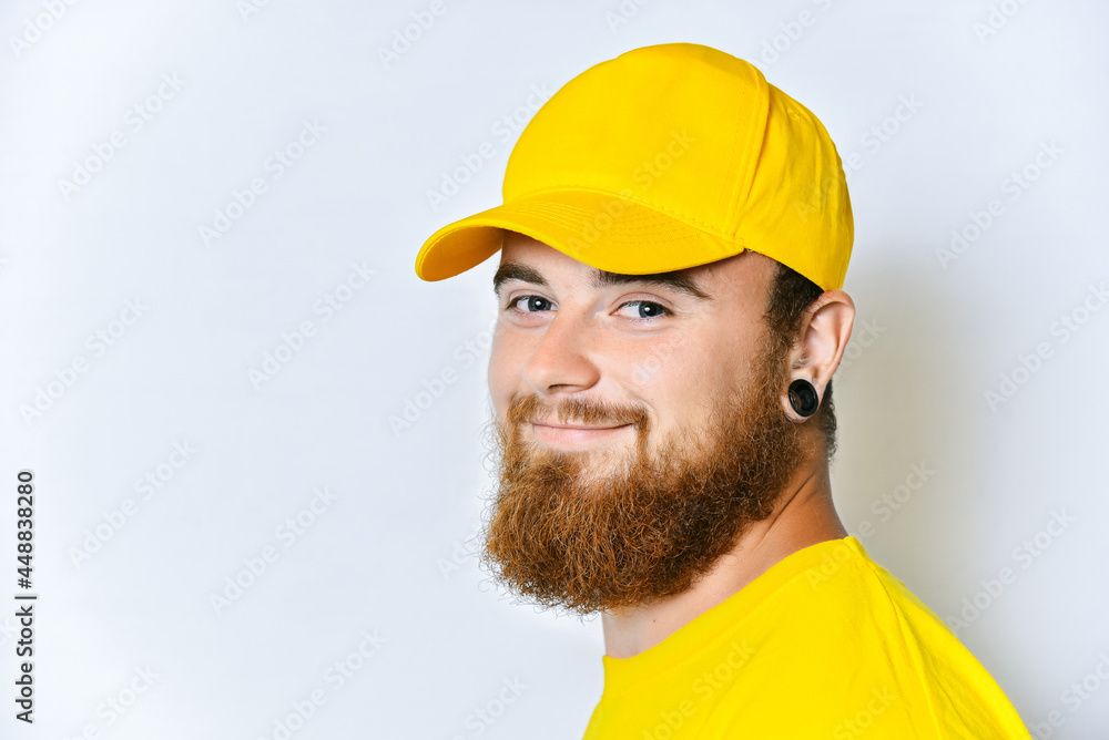 Portrait of a young man with a beard in a yellow uniform on a white background, studio portrait of a delivery service employee