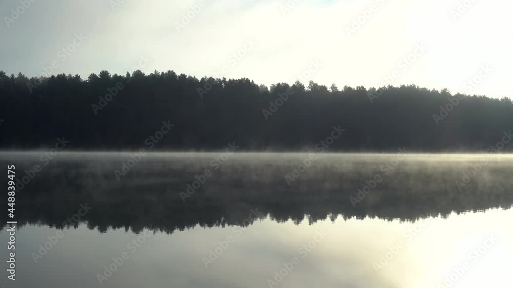 Morning fog blows slowly across a clam lake with forest reflecting in the water. Morning fog blows slowly across a clam lake with forest reflecting in the water.