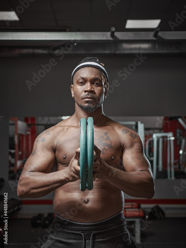 Handsome muscular athletic african american man exercising with weight plates. Training in gym 