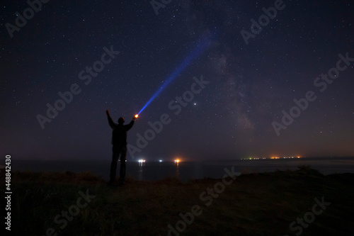 silhouette of man with flashlight beaming ray to Milky Way galaxy