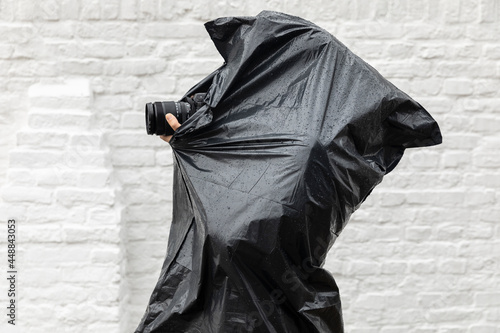 Photographer photographing in the rain while wearing a plastic black waterproof barbage bag as a poncho to protect herself from the bad wet cold weather. Dedication concept