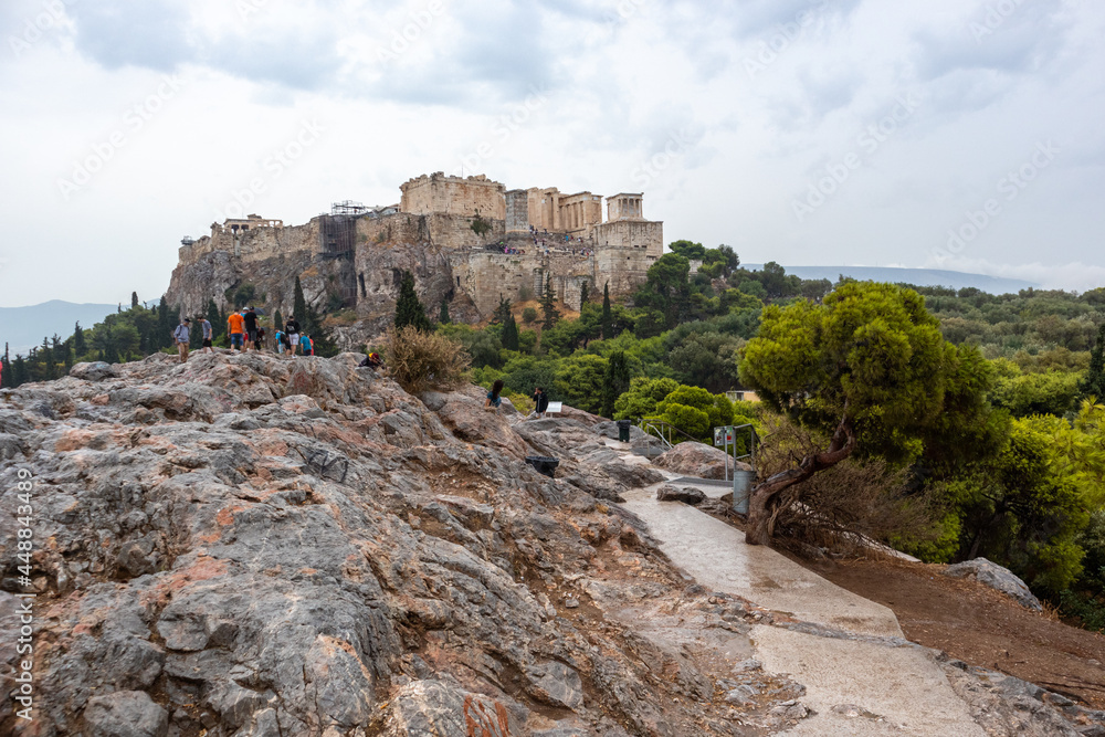 Athens, Greece - September 24, 2019: Acropolis hill (Parthenon, Temples) in greenery on summer cloudy day. Athens historical landmark in city center from rocky Filopappou Hill on cloudy day