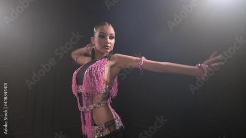 Attractive teenage girl in a beautiful pink black dress professionally dancing ballroom sports dance sambu latino american dances in a dark room filled with smoke photo