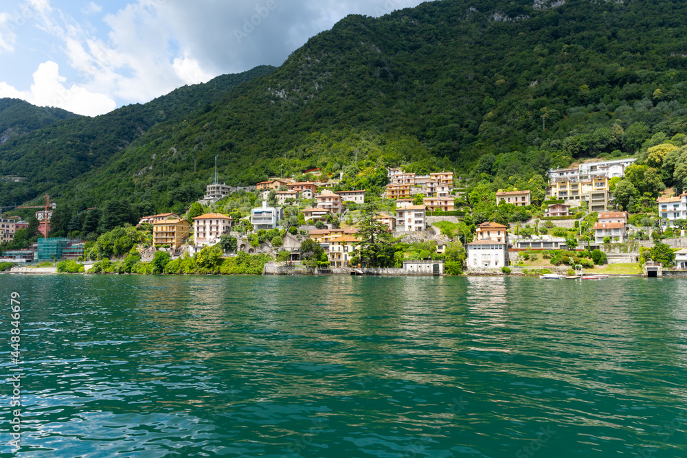 Small town by Lake Como, seen from the lakeside. Beautiful village spread out over the hills, and all the way down to the lake. It is a beautiful sunny summer day