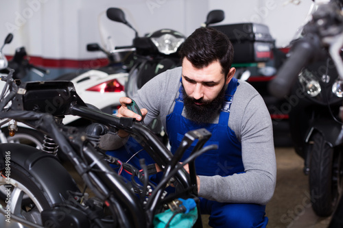 Positive male worker repairing failed scooter in motorcycle workshop
