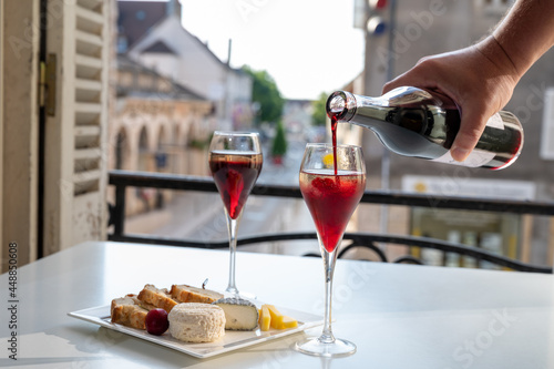 Drinking of Kir Royal,  French aperitif cocktail made  from creme de cassis topped with champagne, typically served in flute glass, with view on old French village © barmalini