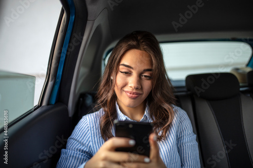 Woman with smartphone on the back seat of a car. Young girl uses a mobile phone in the car. Technology cell phone isolation. Internet and social media. Woman with smartphone in her car. © Dragana Gordic