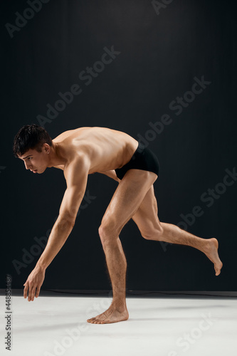 man bodybuilder in black shorts bent knees dark background