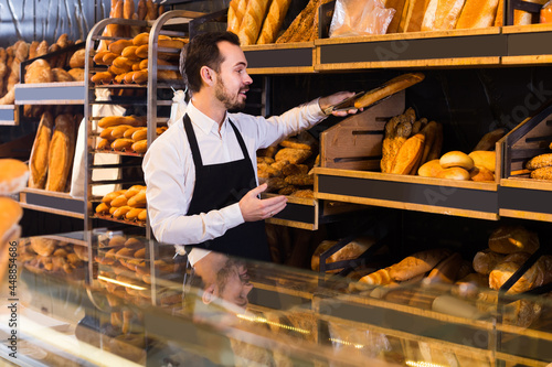 positive spanish male shop assistant demonstrating delicious loaves of bread in bakery