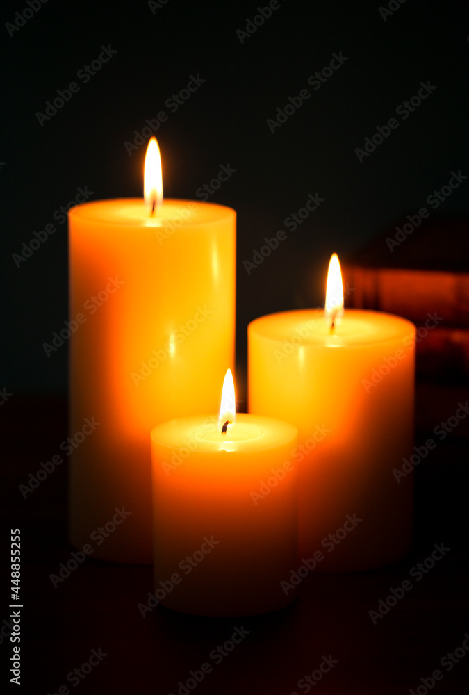 Three Pillar Candles Burning in a Dark Room with a Stack of Antique Books Three Pillar Candles Burning in a Dark Room with a Stack of Antique Books