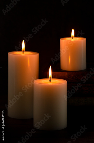 Three Pillar Candles Burning in a Dark Room with a Stack of Antique Books