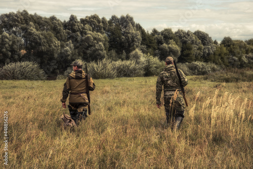 Hunters going through rural field towards forest during hunting season