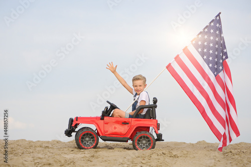 A boy with an American flag in a small toy car.