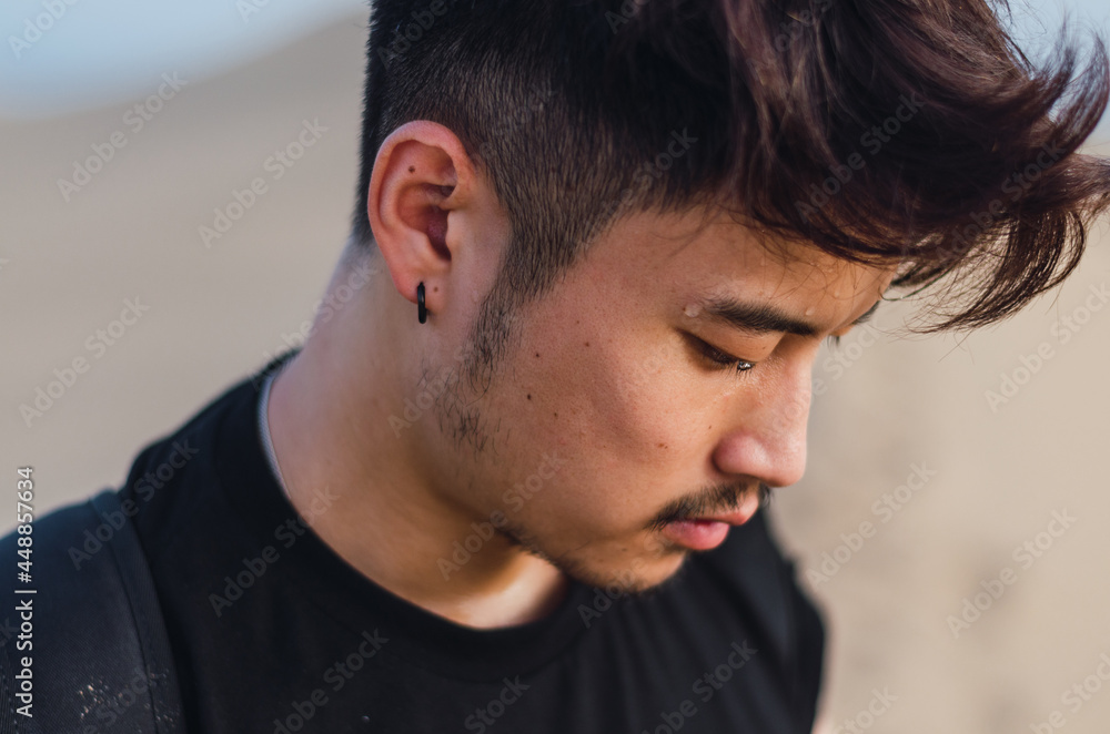 Portrait of young handsome Chinese tourist using phone on the sand dunes in Maspalomas Portrait of young handsome Chinese tourist using phone on the sand dunes in Maspalomas