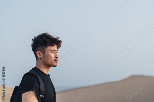 Portrait of young handsome Chinese tourist standing while admiring the sand dunes in Maspalomas