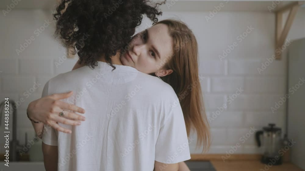 Cute young girl hugging a loved looking over her shoulder at home kitchen