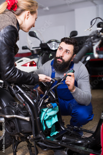 Male worker offering help to female customer to repair motorcycle in workshop