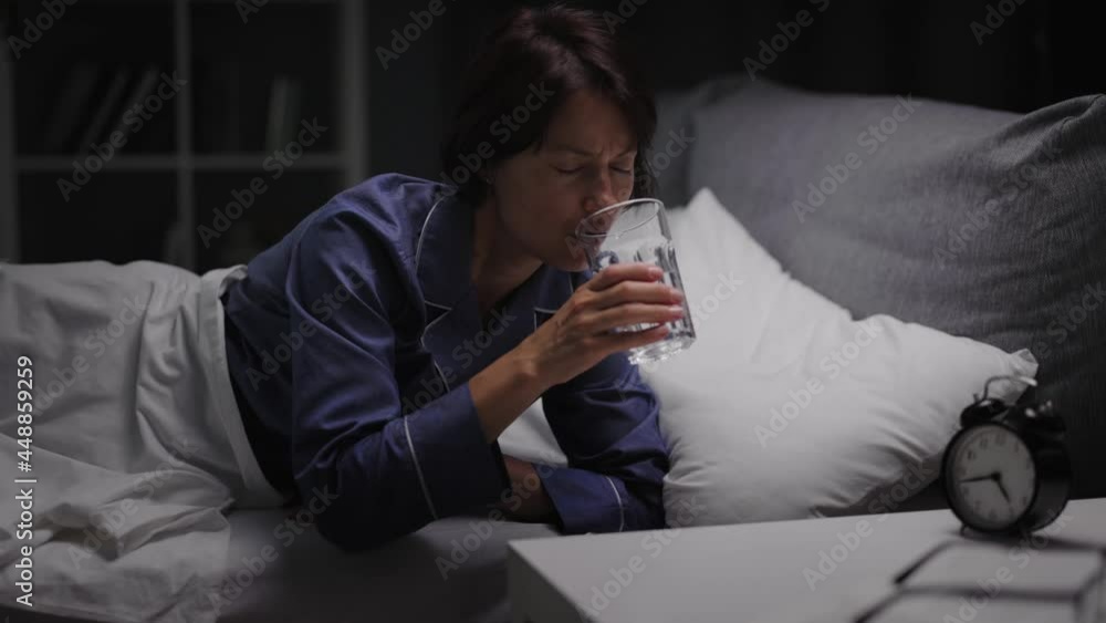 Beautiful dark-haired woman awaking at night for drinking mineral water from glass. Pretty lady in pajamas refreshing at bedroom. Concept of health and hydration. Beautiful dark-haired woman awaking at night for drinking mineral water from glass. Pretty lady in pajamas refreshing at bedroom. Concept of health and hydration.