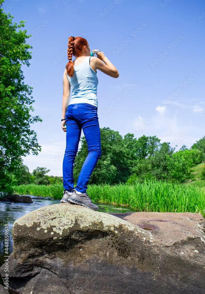 A young girl stands on a stone and drinks water. Rest while traveling. Travel and healthy lifestyle concept. A young girl stands on a stone and drinks water. Rest while traveling. Travel and healthy lifestyle concept.