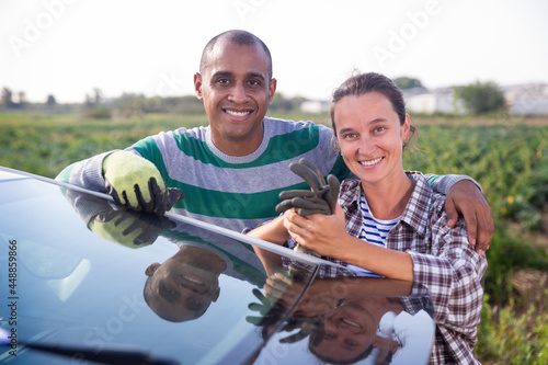 Portrait of successful smiling farmer couple standing outdoors near car on background with vegetable plantation on sunny fall day © JackF