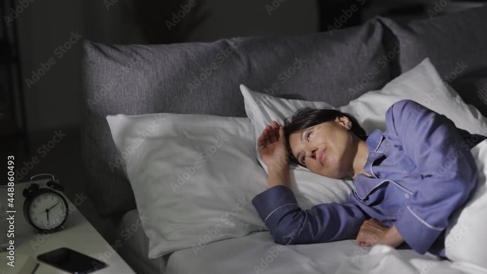 Positive caucasian woman in blue pajamas waking up in morning. Attractive lady with dark hair lying in bed with soft pillows and blanket. Relaxation concept. Positive caucasian woman in blue pajamas waking up in morning. Attractive lady with dark hair lying in bed with soft pillows and blanket. Relaxation concept.