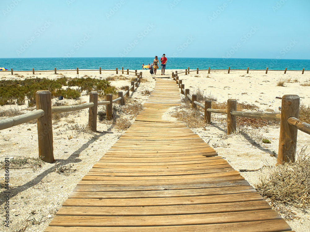 Almería, Spain-July 2, 2021. Wooden path to the beach of Almeria with tourists in the backgroundAlmería, Spain-July 2, 2021. Wooden path to the beach of Almeria with tourists in the background