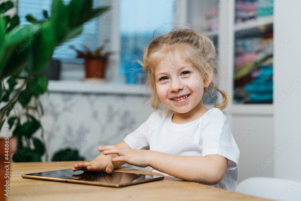 a little girl is sitting at a table with a tablet with her hands raised in the air smiling and happy, experiencing happiness a little girl is sitting at a table with a tablet with her hands raised in the air smiling and happy, experiencing happiness