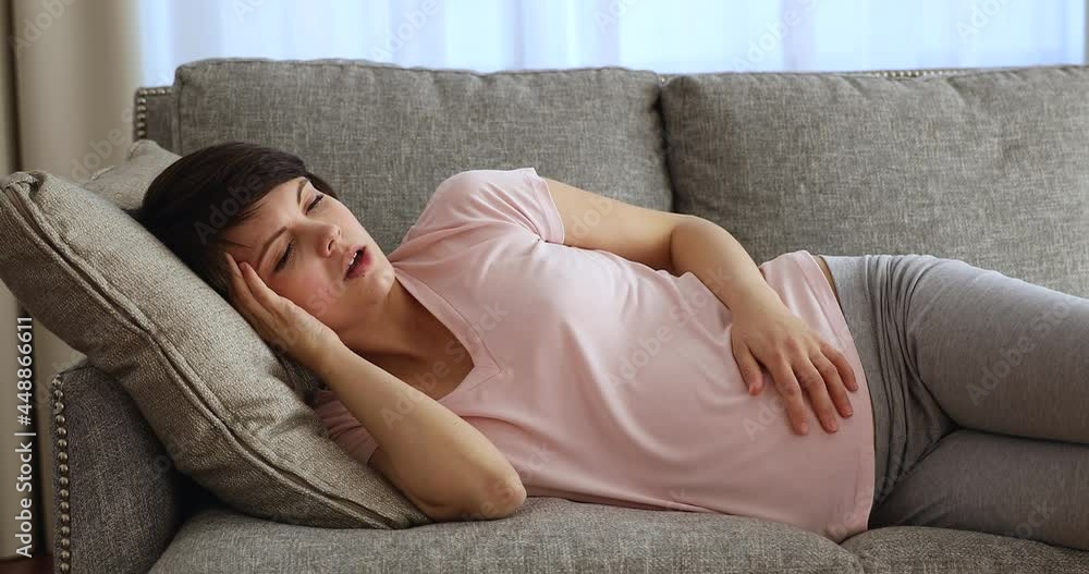 Unhappy tired young pregnant woman suffering from headache or negative thoughts, feeling fear of childbirth, worrying about bad prenatal screening tests results, resting lying on comfortable sofa. Unhappy tired young pregnant woman suffering from headache or negative thoughts, feeling fear of childbirth, worrying about bad prenatal screening tests results, resting lying on comfortable sofa.
