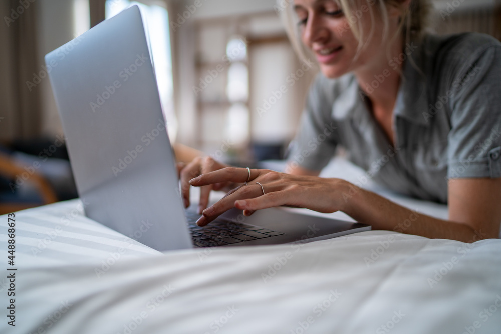 Woman typing on laptop keyboard while lying in bed Woman typing on laptop keyboard while lying in bed