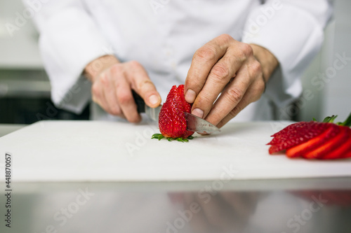 Chef slicing strawberries with kitchen knife photo