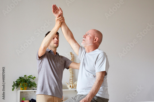 An osteopath lifting and stretching upwards patient's arm