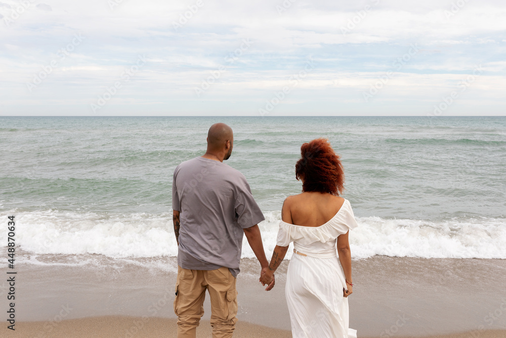 Couple holding hands looking at sea waves Couple holding hands looking at sea waves