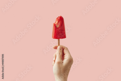 Woman holding bitten strawberry ice cream on stick photo
