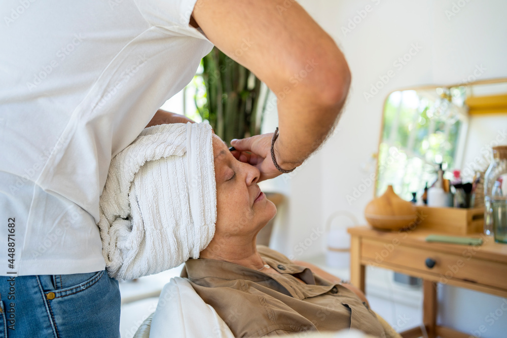 Male beautician plucking senior lady's eyebrows Male beautician plucking senior lady's eyebrows