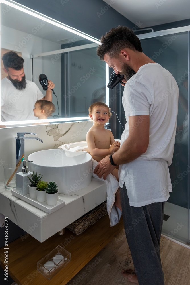 Man drying hair of smiling toddler in bathroom Man drying hair of smiling toddler in bathroom