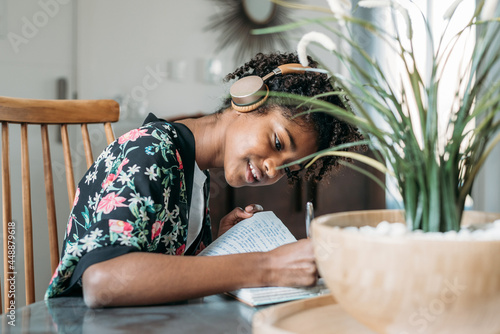 Black teenager listening to music and taking notes in notebook photo