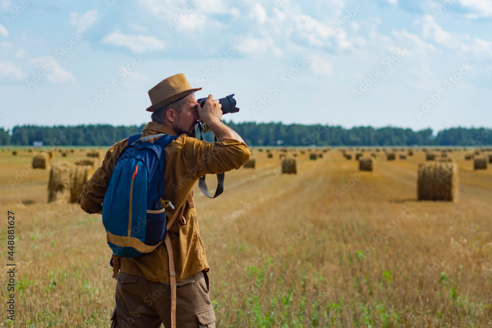 Traveler photographer with a camera in his hand against the background of a field and haystacks.
