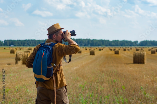 Traveler photographer with a camera in his hand against the background of a field and haystacks. © vadish